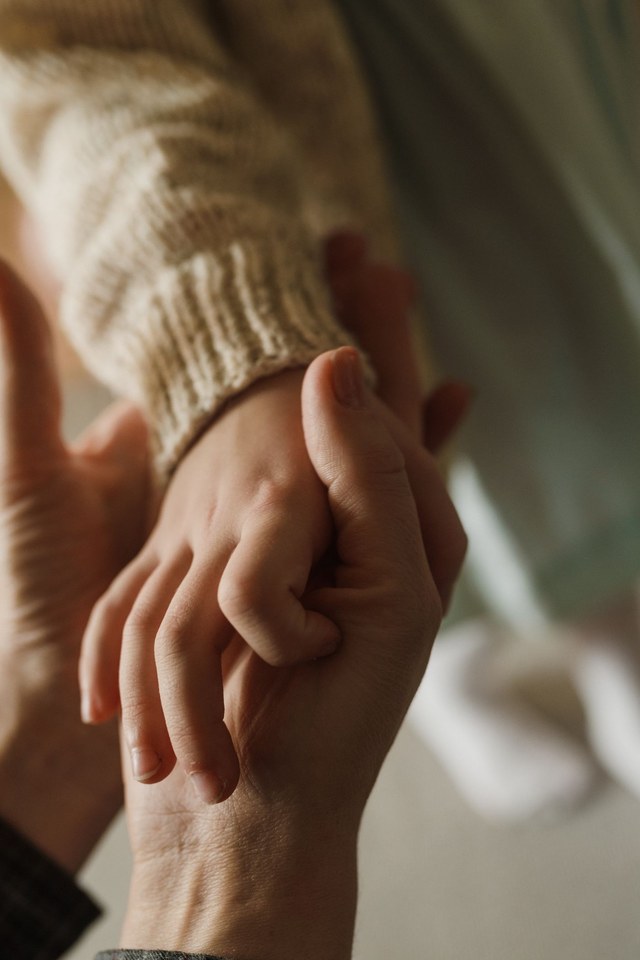 Eine erwachsene Hand hält behutsam die Hand eines Kindes
